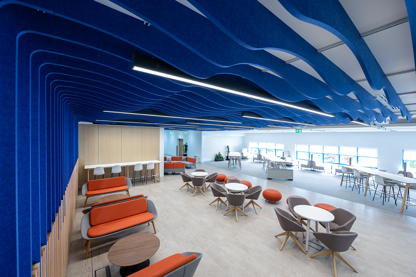 a colourful area in an office with high tables and stools, boothing seatings, sofas and round table with comfortable armchairs around them